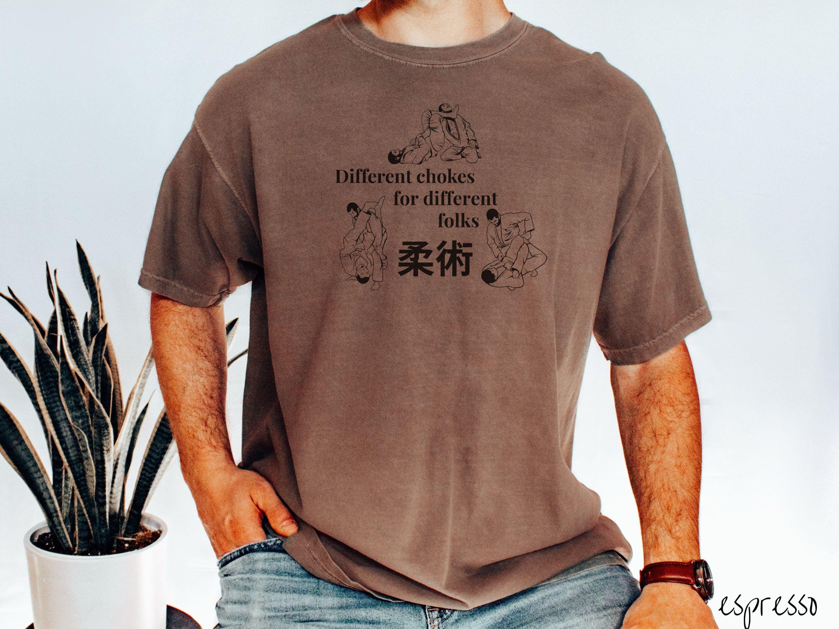 A t-shirt featuring three line art illustrations of Jiu-Jitsu grappling moves. The text reads 'Different chokes for different folks' with Japanese Kanji for 'Jiu-Jitsu' in the center."
